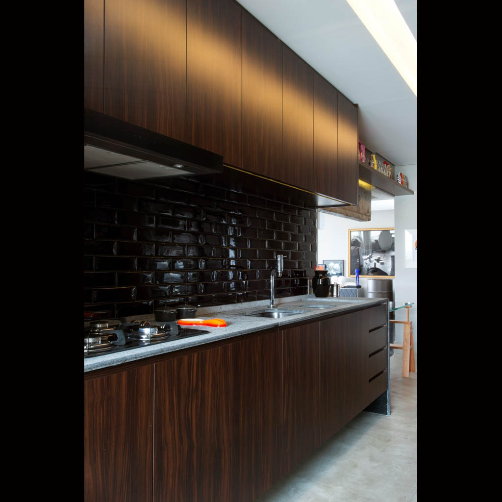 Os armários da cozinha no padrão Jatobá e o revestimento da parede, preto brilhante, contrastam com a bancada em granito São Gabriel
